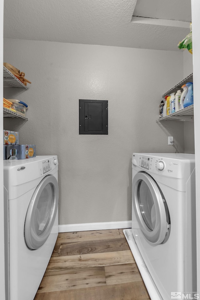 washroom with electric panel, laundry area, washer and clothes dryer, and wood finished floors