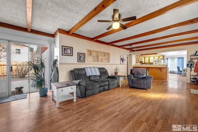 living area featuring beam ceiling, wood finished floors, a wealth of natural light, and a textured ceiling