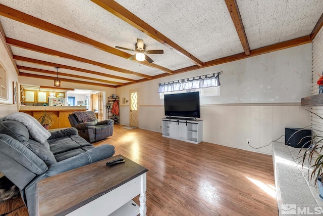 living room with a wainscoted wall, beamed ceiling, wood finished floors, a textured ceiling, and a ceiling fan