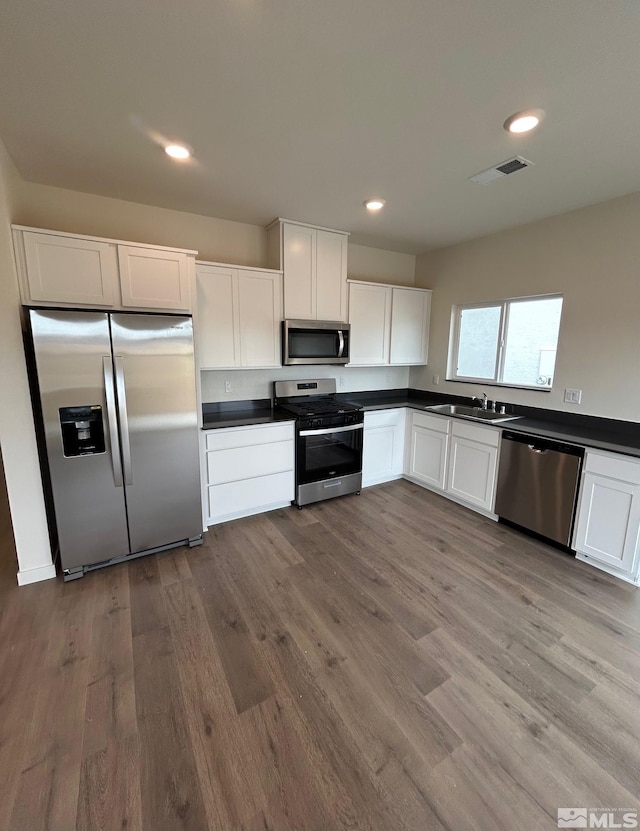 kitchen featuring stainless steel appliances, dark countertops, visible vents, and wood finished floors