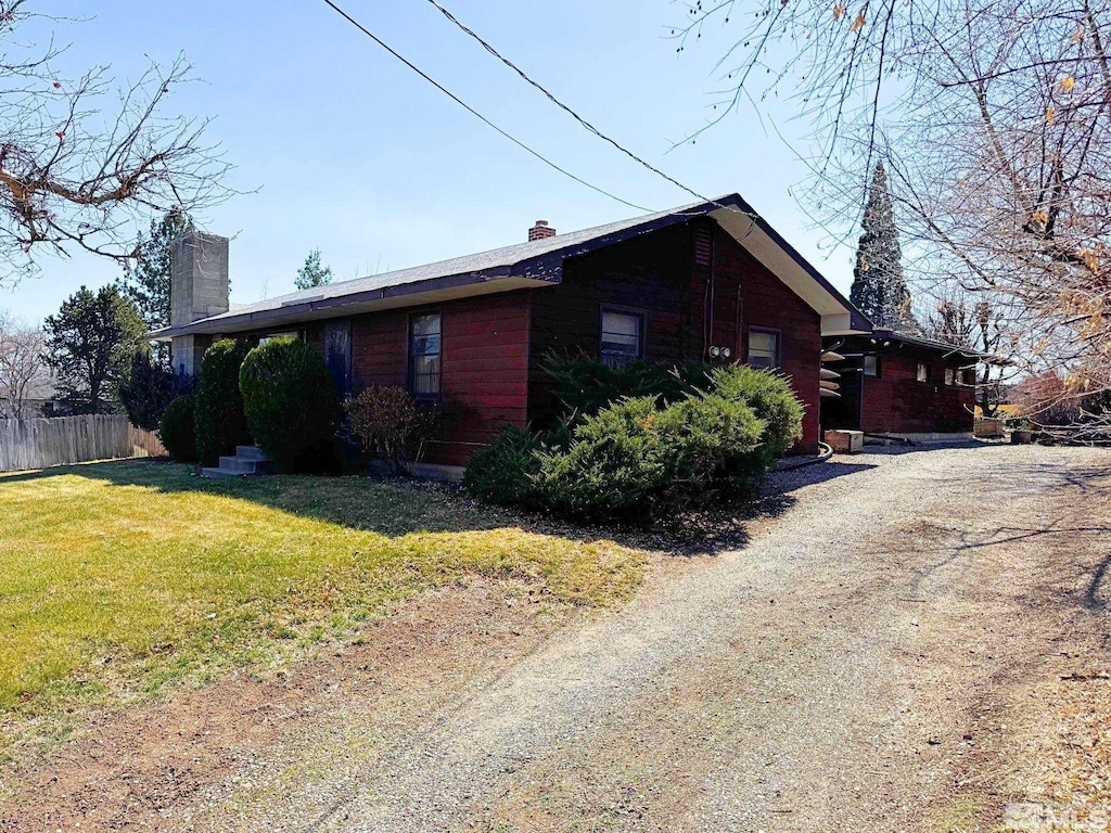 view of side of home featuring a yard, a chimney, dirt driveway, and fence