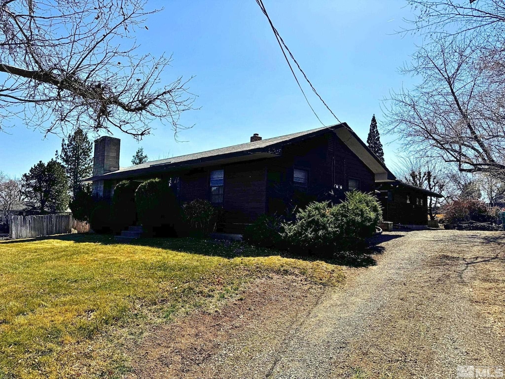 view of home's exterior featuring dirt driveway, a lawn, a chimney, and fence