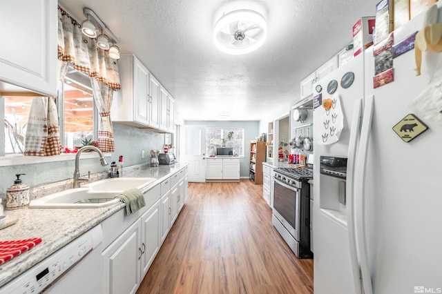 kitchen with light countertops, light wood-style floors, white cabinets, white appliances, and a sink