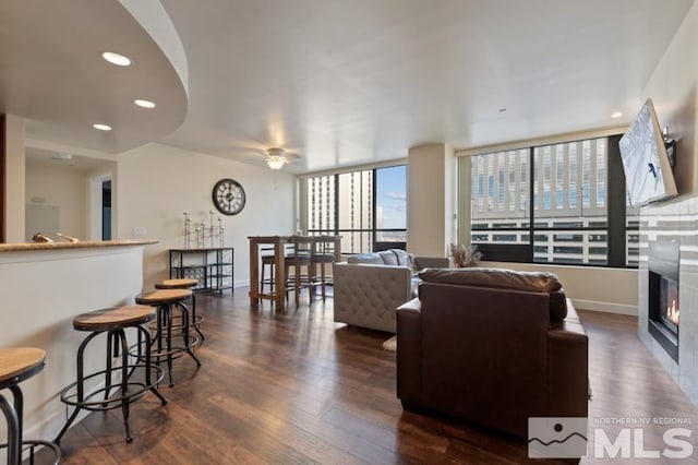 living area with a ceiling fan, baseboards, dark wood finished floors, recessed lighting, and a glass covered fireplace