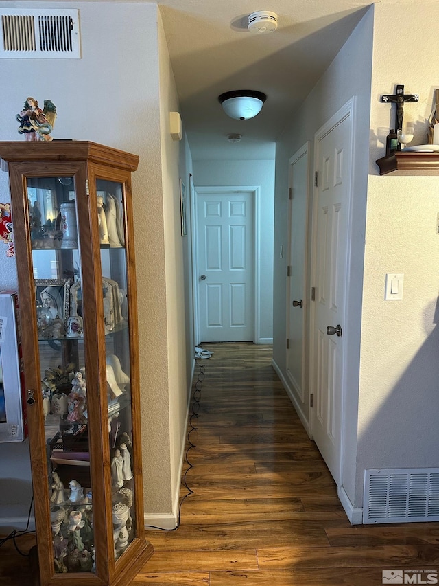 hallway featuring visible vents, baseboards, and wood finished floors