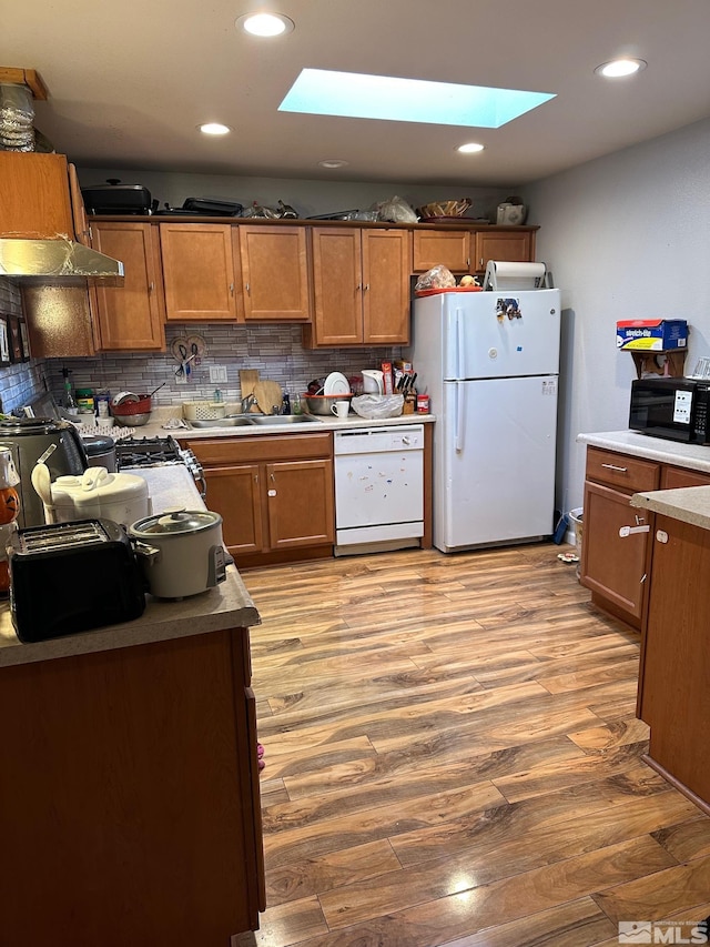 kitchen with decorative backsplash, brown cabinets, light wood-style flooring, white appliances, and a sink