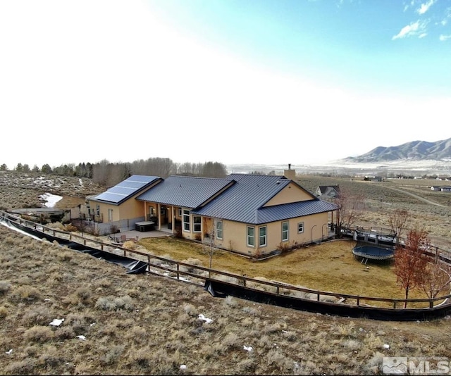 rear view of property featuring a patio, fence, solar panels, a trampoline, and metal roof