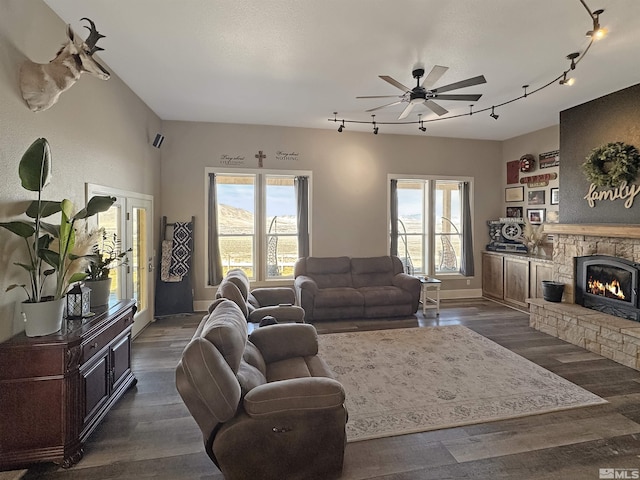 living area with plenty of natural light, dark wood-type flooring, a stone fireplace, and a ceiling fan