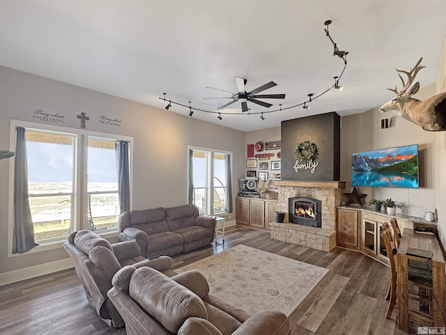 living area featuring ceiling fan, baseboards, a fireplace, rail lighting, and wood finished floors