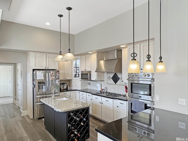 kitchen featuring dark stone countertops, wall chimney exhaust hood, appliances with stainless steel finishes, and a sink