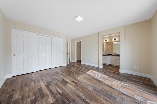 unfurnished bedroom with a closet, baseboards, ensuite bath, and wood finished floors