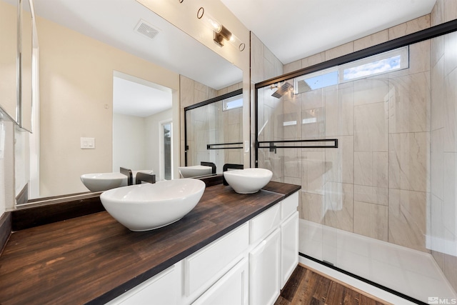 full bath with visible vents, double vanity, a stall shower, wood finished floors, and a sink