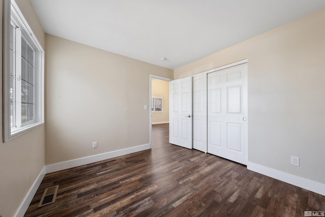 unfurnished bedroom featuring dark wood finished floors, baseboards, visible vents, and a closet