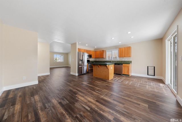 kitchen with a kitchen island, open floor plan, a breakfast bar area, appliances with stainless steel finishes, and dark wood-style flooring