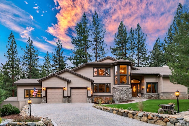 view of front of home with decorative driveway, stone siding, a front lawn, and an attached garage