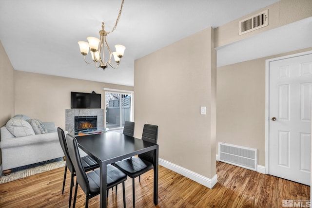 dining space with a fireplace, wood finished floors, visible vents, and baseboards