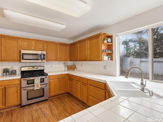 kitchen with light wood-style flooring, tasteful backsplash, appliances with stainless steel finishes, and a sink