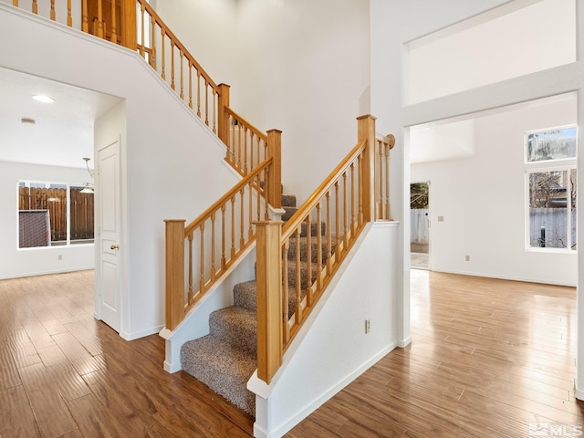 stairs with plenty of natural light, a towering ceiling, and hardwood / wood-style floors