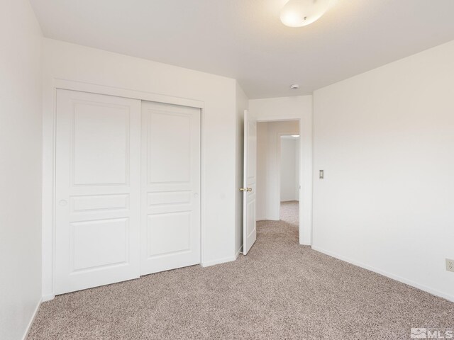 unfurnished bedroom with baseboards, a closet, and light carpet