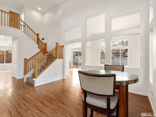 dining area with stairway, wood finished floors, and a towering ceiling