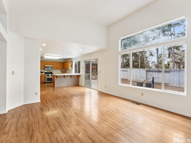 unfurnished living room with visible vents, baseboards, recessed lighting, a sink, and light wood-style floors