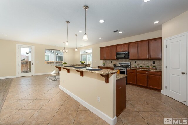 kitchen with visible vents, stainless steel gas stove, a breakfast bar, black microwave, and decorative backsplash