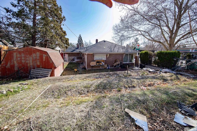 rear view of property with brick siding, fence, a chimney, an outbuilding, and a storage unit