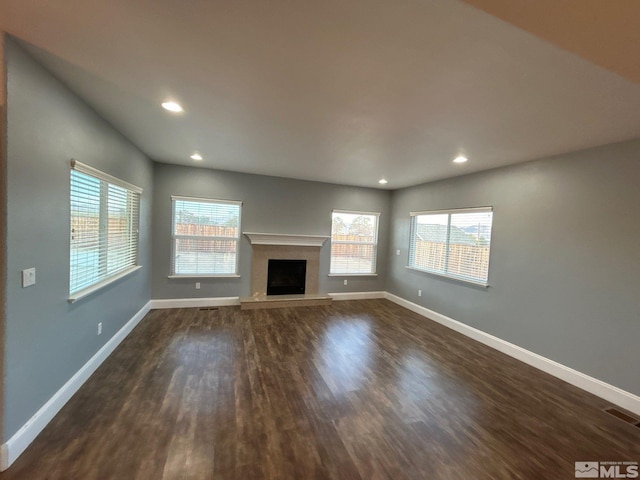 unfurnished living room with a premium fireplace, plenty of natural light, baseboards, and dark wood-style flooring