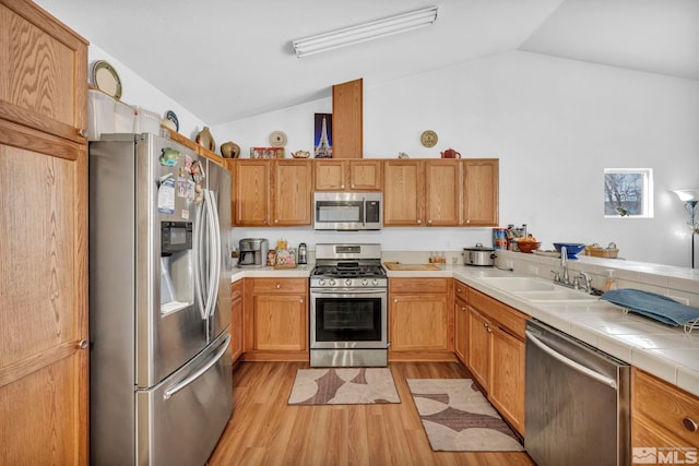 kitchen with lofted ceiling, a sink, tile counters, appliances with stainless steel finishes, and light wood-type flooring