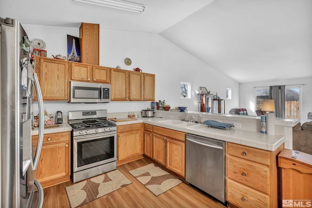 kitchen featuring a sink, stainless steel appliances, light wood-style floors, a peninsula, and vaulted ceiling