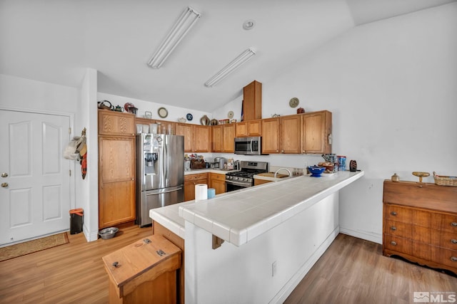 kitchen featuring tile counters, lofted ceiling, a peninsula, light wood-style floors, and stainless steel appliances