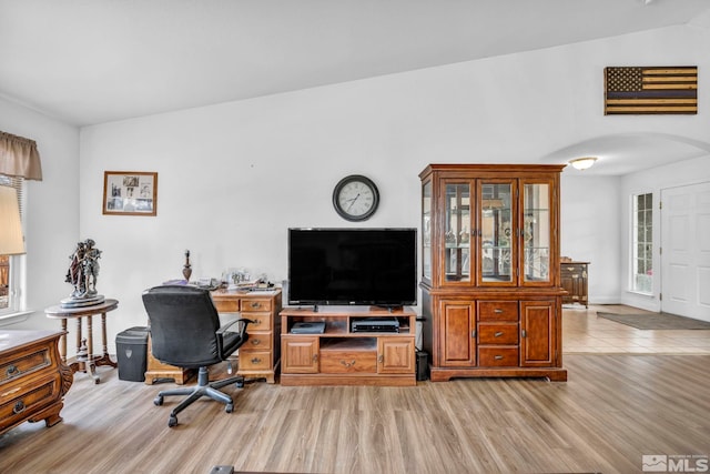 office featuring baseboards, arched walkways, vaulted ceiling, and light wood finished floors