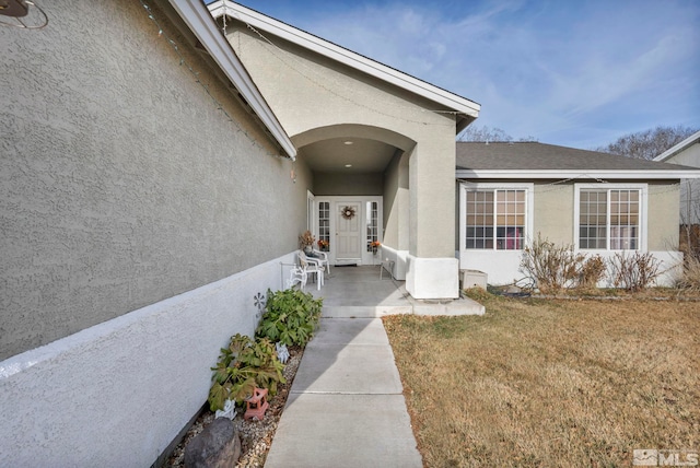 view of exterior entry featuring stucco siding and a yard