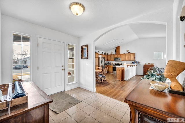 foyer entrance featuring lofted ceiling, light tile patterned floors, baseboards, and arched walkways