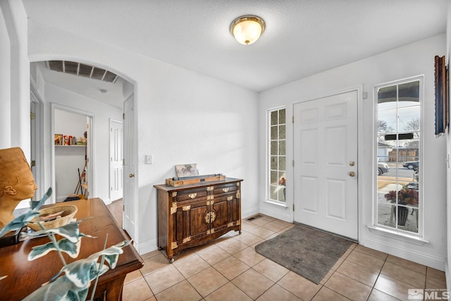 entryway featuring light tile patterned floors, visible vents, arched walkways, and baseboards