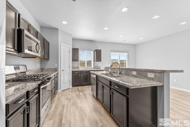 kitchen with light wood-type flooring, a kitchen island with sink, a sink, recessed lighting, and appliances with stainless steel finishes