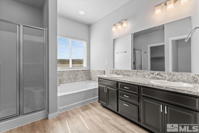 full bathroom featuring a shower stall, a garden tub, wood finished floors, and a sink