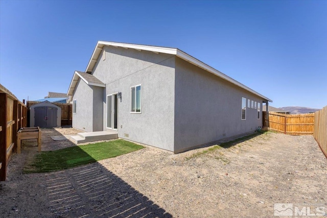 rear view of house featuring an outbuilding, a storage unit, a fenced backyard, and stucco siding