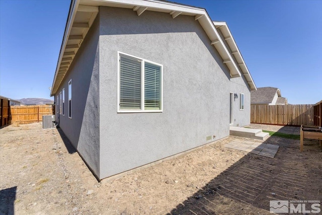 rear view of property featuring central AC unit, stucco siding, and a fenced backyard