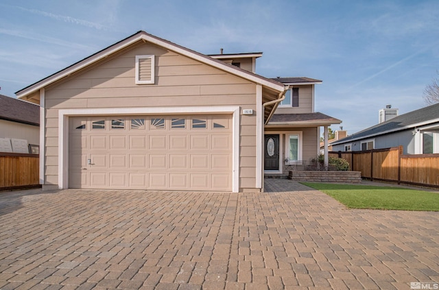 traditional-style home with decorative driveway, an attached garage, and fence