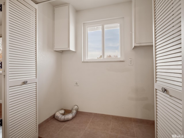 clothes washing area featuring electric dryer hookup, baseboards, cabinet space, and tile patterned flooring