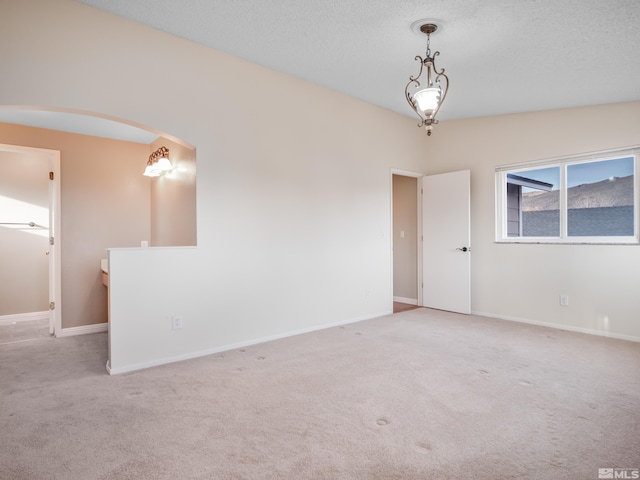 carpeted empty room with arched walkways, a textured ceiling, and baseboards