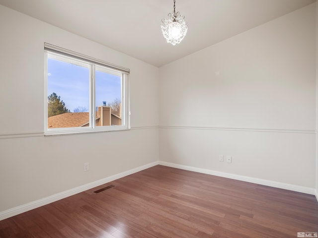 empty room featuring visible vents, baseboards, a notable chandelier, and wood finished floors