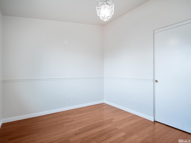 empty room with a notable chandelier, wood finished floors, and baseboards