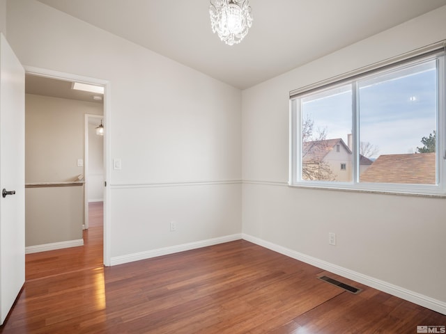 unfurnished room with wood finished floors, visible vents, and baseboards