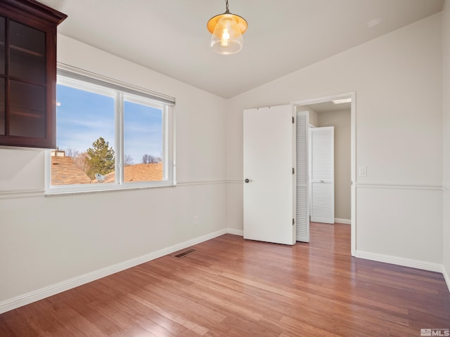 spare room with visible vents, baseboards, light wood-type flooring, and lofted ceiling