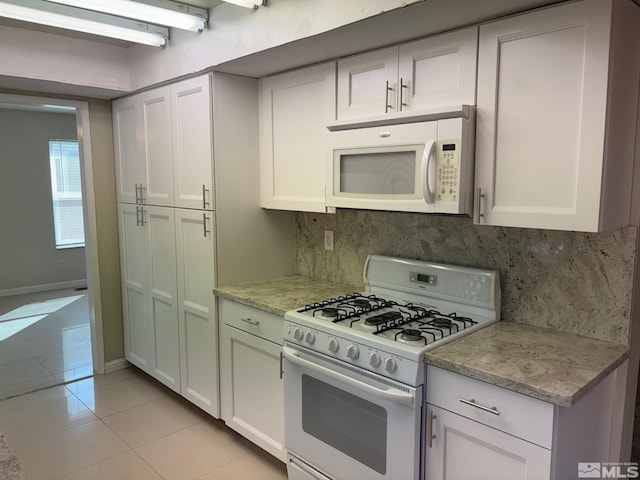 kitchen with tasteful backsplash, light stone countertops, light tile patterned floors, white cabinets, and white appliances