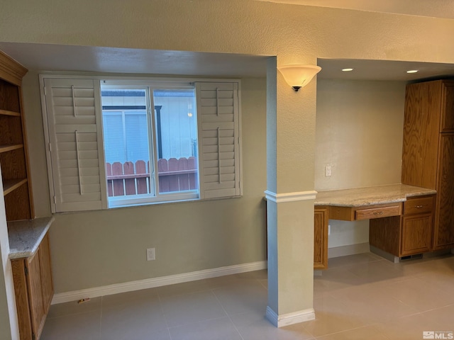 unfurnished office featuring light tile patterned flooring, built in desk, and baseboards