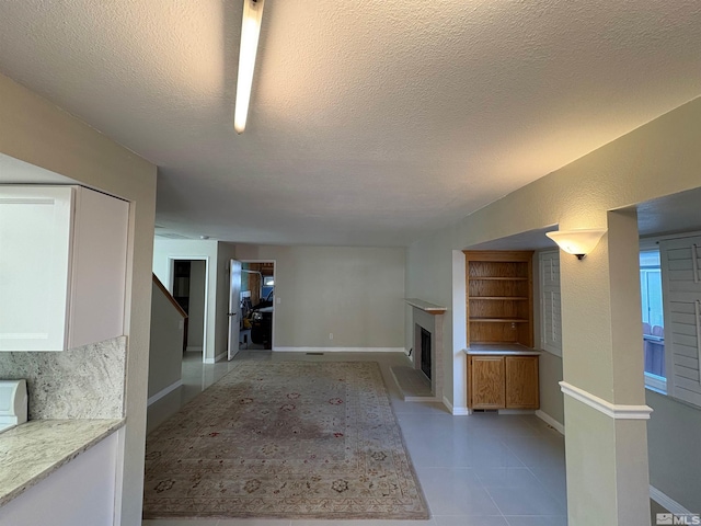 unfurnished living room with light tile patterned floors, built in shelves, baseboards, a fireplace with raised hearth, and a textured ceiling