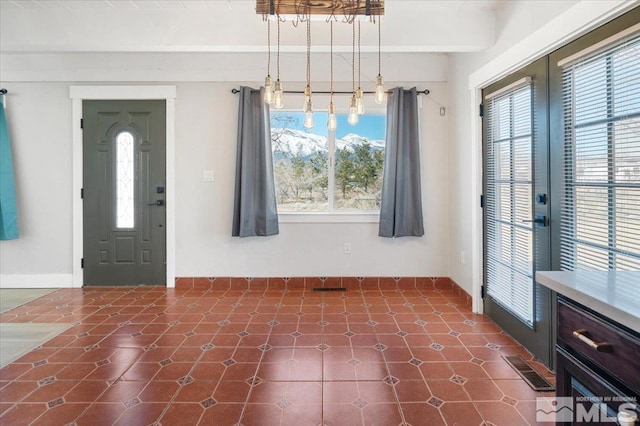 foyer entrance with beamed ceiling, a healthy amount of sunlight, visible vents, and baseboards